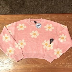 Pink knitted cropped sweater with daisy flower pattern.